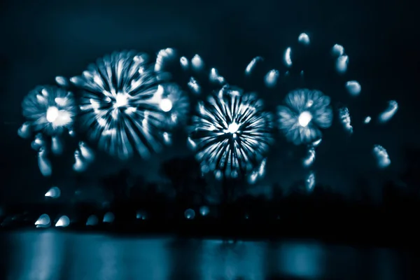Abstract, blurry, bokeh-style colorful photo of fireworks in a blue tone above the river — Stock Photo, Image