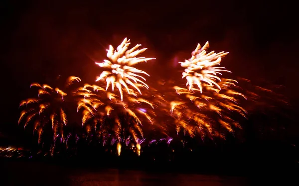 Abstract, blurry, bokeh-style colorful photo of fireworks in a red tone above the river — Stock Photo, Image