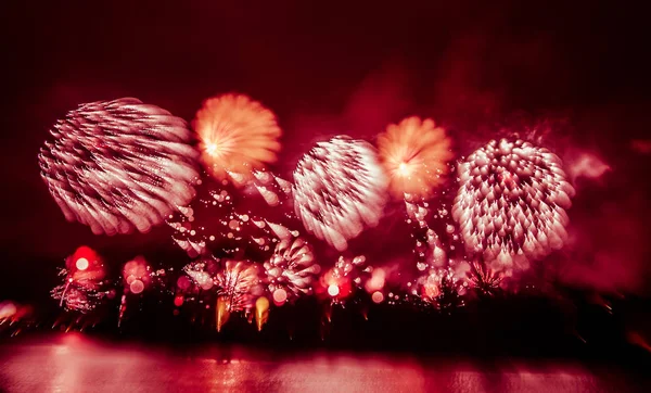 Photo colorée abstraite, floue et de style bokeh de feux d'artifice dans un ton rouge au-dessus de la rivière — Photo