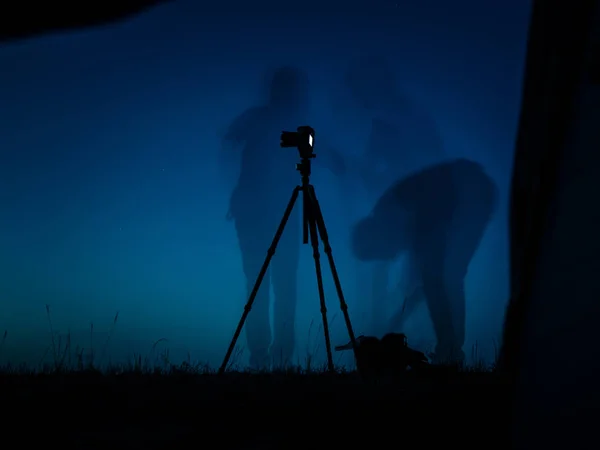 Bir fotoğrafçı eylem sanatsal uzun pozlama fotoğraf. Birden çok siluetleri ve kamera BM tripod. Gece çadırda bir görünüm — Stok fotoğraf