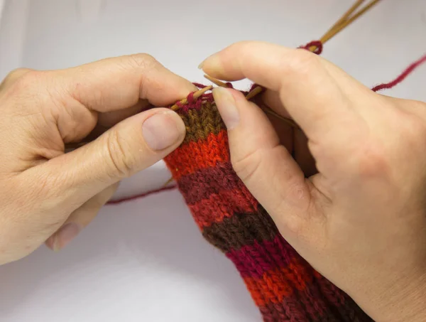 Een vrouw breien rode wollen sokken. Breien dicht omhoog op een witte achtergrond. Hand ambachten. Gedetailleerde weergave van een vaardigheid breien. — Stockfoto