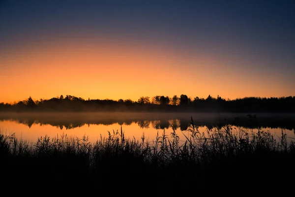 Um belo nascer do sol num lago com uma névoa. Bela manhã em zonas húmidas na Letónia. Paisagem de outono em cores brilhantes . — Fotografia de Stock