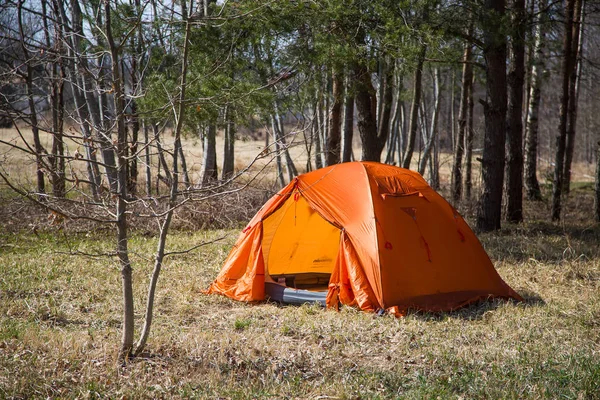 An orange tent built on the bank of the river. Hiking camp in the spring. Early spring scenery.