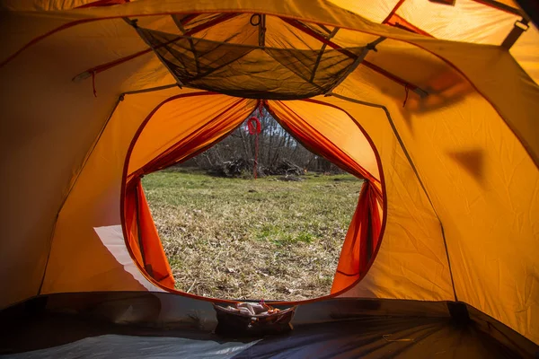 A look through the entrance of the tent. Orange camping tent in an early spring. Exit door.