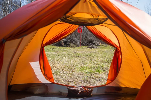 A look through the entrance of the tent. Orange camping tent in an early spring. Exit door.