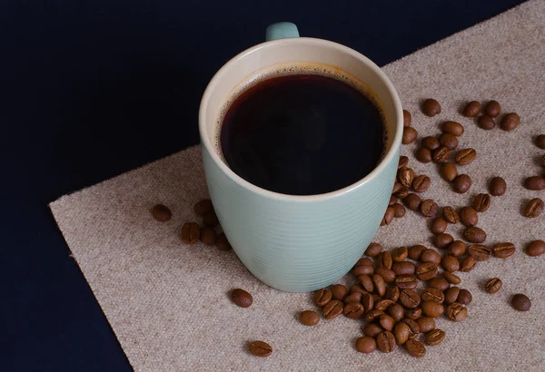 Coffee without foam in a cup and whole grains of Colombian coffee on a dark table. The charge of energy in the morning.