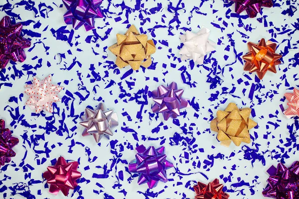 Hediye yayları ve konfeti şenlikli parlak bir arka plan. Mavi kağıt parçalarıyla birlikte renkli hediye kurdele düğümleri. Bayram kompozisyonu. Noel, doğum günü dekoratifi tebrik kartı için renkli arkaplan. — Stok fotoğraf