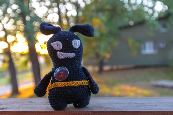 Handmade black crocheted toy walks on brick pathway, observes the street in autumn.