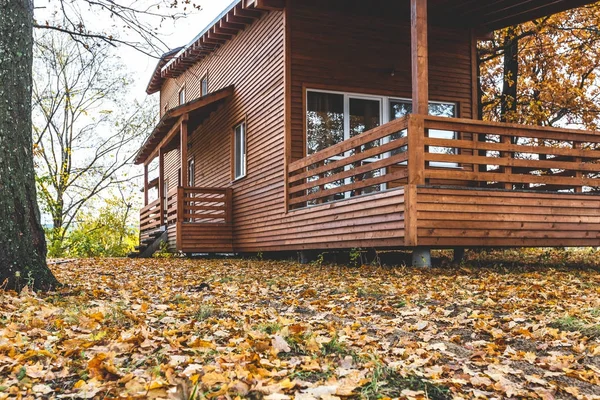 Red wooden cottage on piles in oak forest in autumn. Very beautiful relaxing place, ideal for weekend and vacation rental. Retreat place near river. Scandinavian wooden house contemporary exterior.