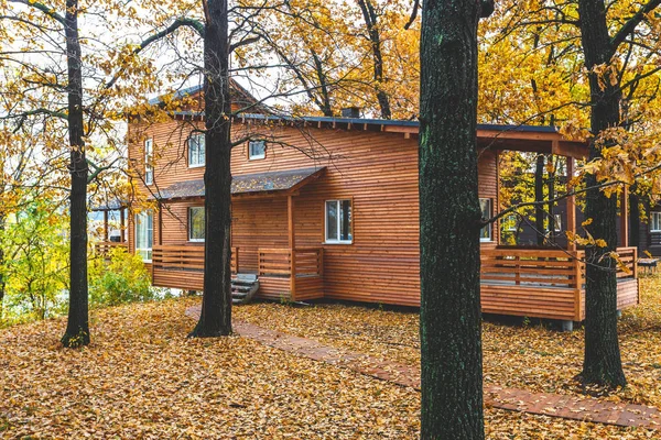 Red wooden cottage on piles in oak forest in autumn. Very beautiful relaxing place, ideal for weekend and vacation rental. Retreat place near river. Scandinavian wooden house contemporary exterior.