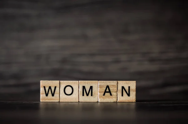 A palavra mulher compõe-se de painéis quadrados de madeira leves em uma escuridão — Fotografia de Stock