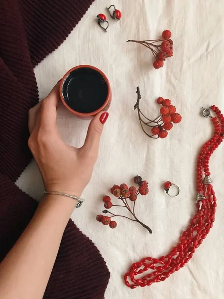 Vintage de la moda plana con la mano sosteniendo la taza de té, accesorios femeninos, bufanda, cuentas rojas, pendientes, anillo y remo, vista superior — Foto de Stock