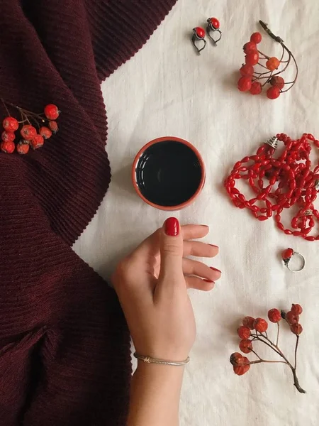 Винтажная модная квартира лежала с рукой держа чашку чая, женские аксессуары, шарф, красные бусины, серьги, кольцо и рябина, вид сверху — стоковое фото