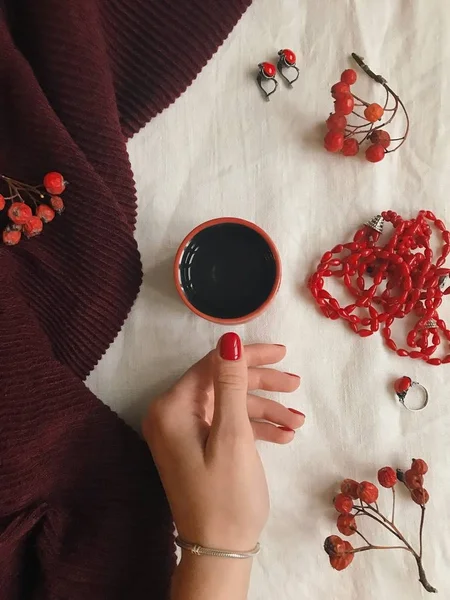Vintage de la moda plana con la mano sosteniendo la taza de té, accesorios femeninos, bufanda, cuentas rojas, pendientes, anillo y remo, vista superior — Foto de Stock