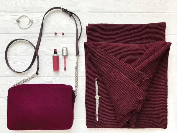 Women fashion cloth and accessories. Flat lay female winter casual style look with Winter scarf, small bag, lipstick, earrings, bracelet, watches in marsala color. Top view.