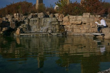 Sıcak sonbahar günü güneşin sıcaklığına zevk suyu akan tarafında bir kitap okuma