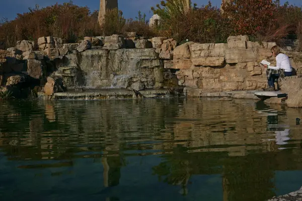 Sıcak sonbahar günü güneşin sıcaklığına zevk suyu akan tarafında bir kitap okuma