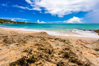 Taş kaya sarı zemin kıyı şeridi ve parlak renkli gökyüzü beyaz bulutlar ile karşı masmavi deniz kıyısında.
