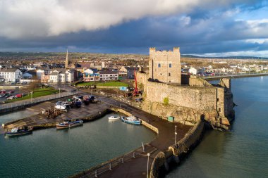 Ortaçağ Norman Kalesi, Carrickfergus 'ta tekne rampası ve dalga kırıcısı olan liman Belfast, Kuzey İrlanda, İngiltere yakınlarında. Kışın gün batımında hava manzarası. Kasaba ve fırtınalı bulutlar arka planda