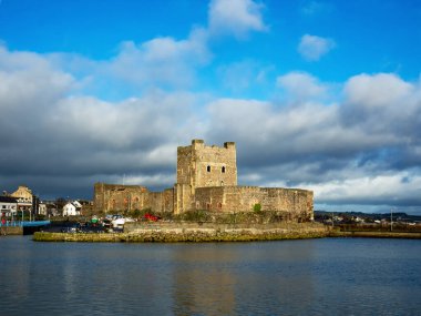 Kuzey İrlanda, Belfast yakınlarındaki Carrickfergus 'taki Ortaçağ Norman Kalesi' nde kışın marina ile birlikte. Kara fırtınalı bulutlu dramatik bir gökyüzü. Gün batımı ışığı