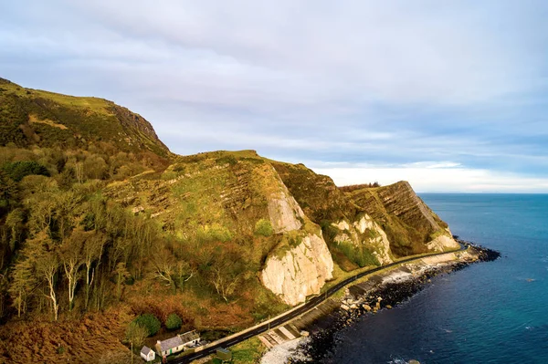 Northern Ireland, UK. Atlantic coast. Cliffs and Antrim Coast Road, a.k.a. Causeway Coastal Route. One of the most scenic coastal roads in Europe. Aerial view near Garron Point in sunrise light