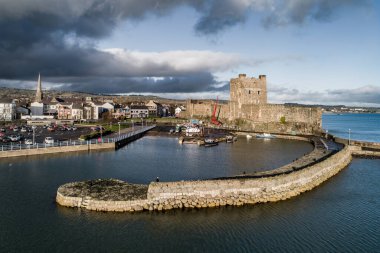 Ortaçağ Norman Kalesi, Carrickfergus 'ta tekne rampası ve dalga kırıcısı olan liman Belfast, Kuzey İrlanda, İngiltere yakınlarında. Kışın gün batımında hava manzarası. Kasaba ve fırtınalı bulutlar arka planda