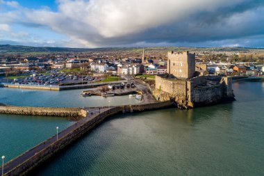 Ortaçağ Norman Kalesi, Carrickfergus 'ta tekne rampası ve dalga kırıcısı olan liman Belfast, Kuzey İrlanda, İngiltere yakınlarında. Kışın gün batımında hava manzarası. Kasaba ve fırtınalı bulutlar arka planda