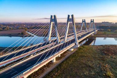 Polonya 'nın Krakow kentindeki Vistula Nehri üzerinde üç şeritli geniş yolları olan ve gündoğumunda suya yansıyan yeni modern çift kablolu köprü. Krakow çevresindeki çevre yolunun bir parçası. Hava görünümü