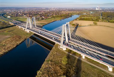 Polonya 'nın Krakow kentindeki Vistula Nehri üzerinde üç şeritli geniş yolları olan ve gündoğumunda suya yansıyan yeni modern çift kablolu köprü. Krakow çevresindeki çevre yolunun bir parçası. Hava görünümü