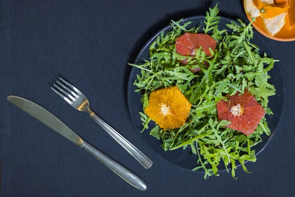 Salade verte de roquette sur une assiette avec tranches d'orange et grappin — Photo
