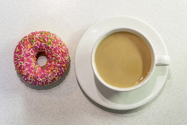 One donut bright colored lies next to me with a cup of coffee wi