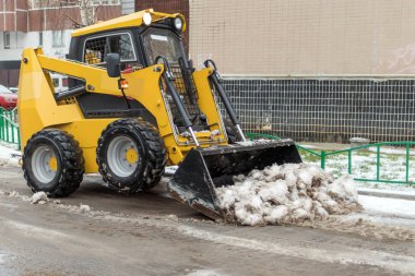 Küçük sarı buldozer kar sokaktan temizler. 