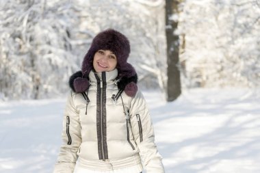 Gülümseyen kadın ormanda bir kürk şapka duruyor ve 