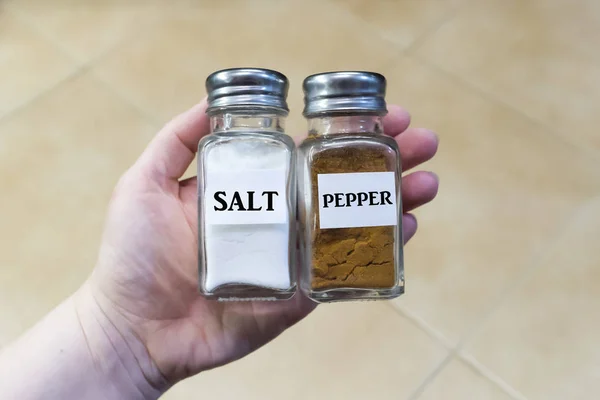 Hand holds cans with spices, salt and pepper, background cooker — Stock Photo, Image