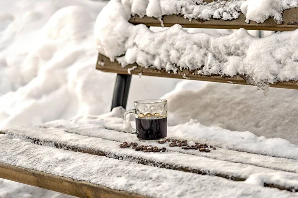 Tasse mit schwarzem Espresso steht im Schnee, eine Holzbank — Stockfoto