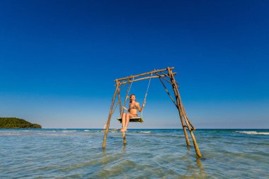 Genç seksi kadın Vietnam 'daki tropikal ada Phu Quoc' ta salıncakta. Sıcak güneşli bir günde Sao sahilinde turist.