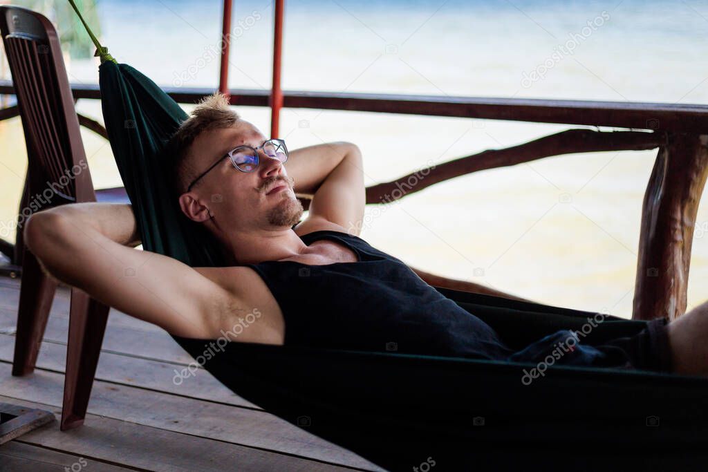 Young goodlooking man lying in a hammock in local seafood restaurant in  fishermans village Ham Ninh, tropical Phu Quoc island (Bai Thom area) in Vietnam. Holidays chillout