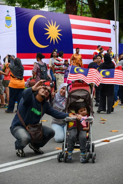 Malezya bayrağı önünde ailesiyle selfie çeken bir adam. — Stok fotoğraf