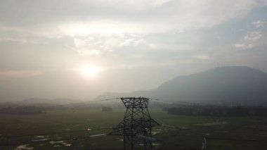 Çeltik tarlasında arka plan tepesi olan hava manzaralı elektrik kulesi.