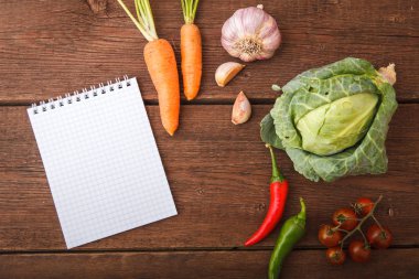 Bir not defteri ile taze sebze ahşap bir arka plan üzerinde yalan. Cabb