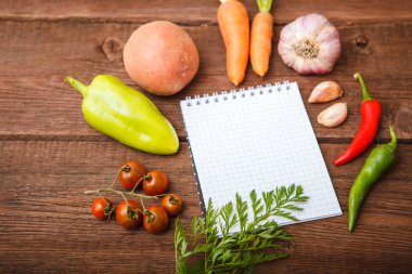 Bir not defteri ile taze sebze ahşap bir arka plan üzerinde yalan. Bulg