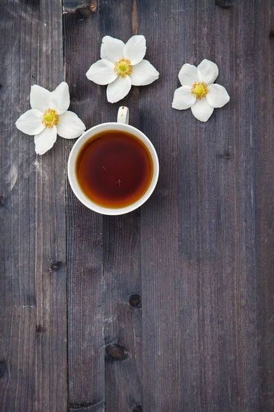 Κινούμενο σχέδιο λευκό λουλούδια με ένα φλιτζάνι τσάι σε ένα ξύλινο υπόβαθρο — Φωτογραφία Αρχείου