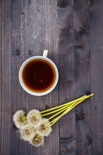 Dandelion flowers with a cup of tea on a wooden background — Stock Photo, Image