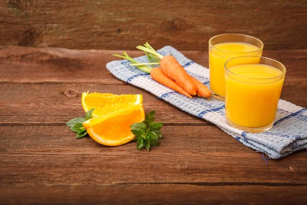 Refreshing orange-carrot juice in a glass on a wooden background
