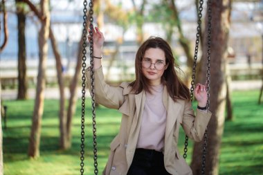 Gözlüklü şık bir kızın portresi, yakın plan. Boş zaman. Güzel bir kadın salıncakta otururken kameraya bakıyor..