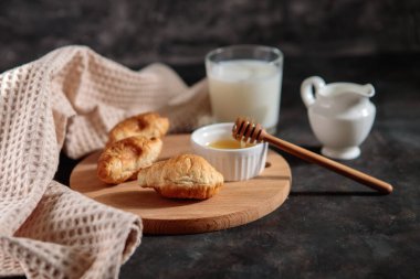 Ballı ve sütlü kruvasanlar, yakın plan, koyu arka plan. Fransız kahvaltısı. Mesaj için yer var. Tatlı.