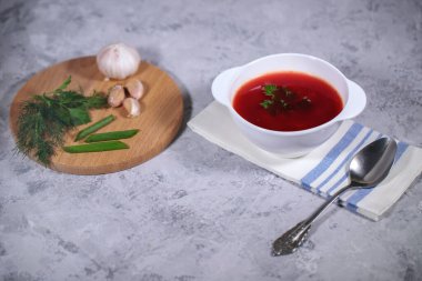 Masanın üzerinde pancar çorbası olan bir tabak, tahtanın yanında maydanoz, dereotu, yeşil soğan ve sarımsak var. Lezzetli ve sağlıklı bir öğle yemeği..