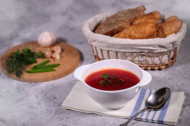 Masanın üzerinde pancar pancar çorbası olan bir tabak, yanında maydanoz, dereotu, yeşil soğan ve sarımsak ve ekmekle birlikte bir sepet. Lezzetli ve sağlıklı bir öğle yemeği..