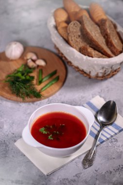 Masanın üzerinde pancar pancar çorbası olan bir tabak, yanında maydanoz, dereotu, yeşil soğan ve sarımsak ve ekmekle birlikte bir sepet. Lezzetli ve sağlıklı bir öğle yemeği..
