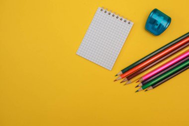 Renkli kalemler, kalemtraş makinesi ve sarı arka planda beyaz bir not defteri, yazı için yer. Düz yatıyordu. kırtasiye.